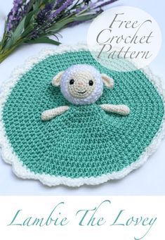 a crocheted sheep sitting on top of a green rug next to lavender flowers