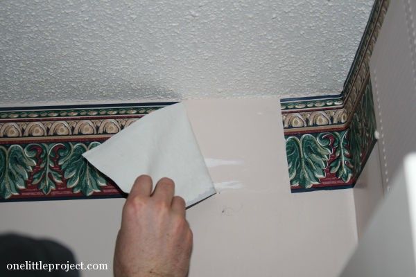 a person wiping up some paper on the wall in front of a ceiling tile border