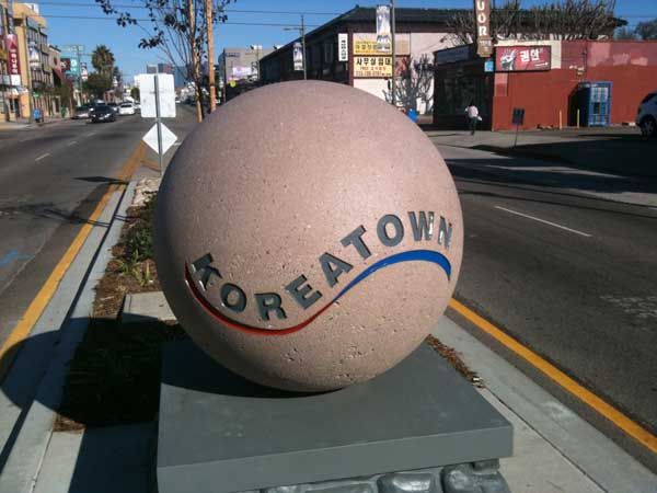 a large rock sitting on the side of a road next to a street with buildings