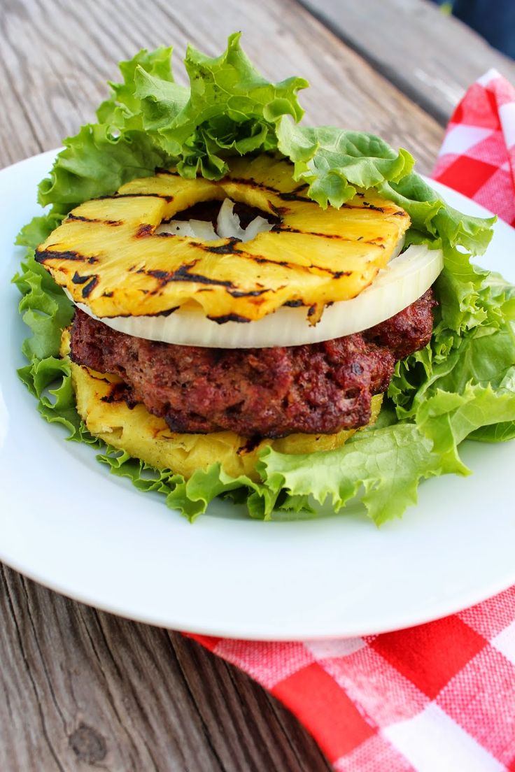 a hamburger with lettuce and pineapple slices on it sitting on a white plate