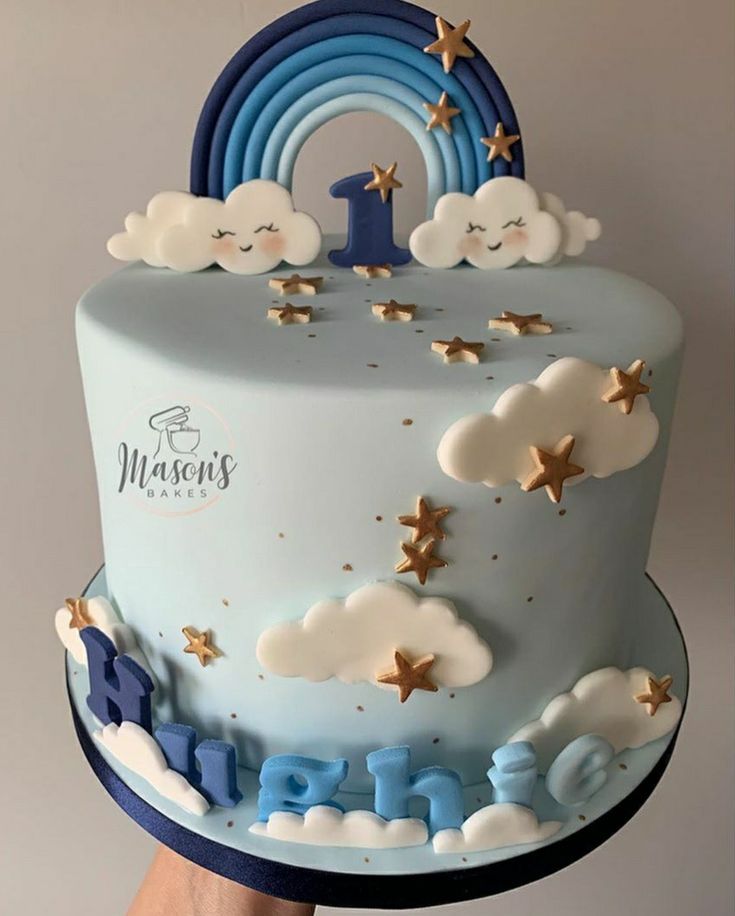 a blue cake with gold stars and clouds on the top is being held up by a person's hand