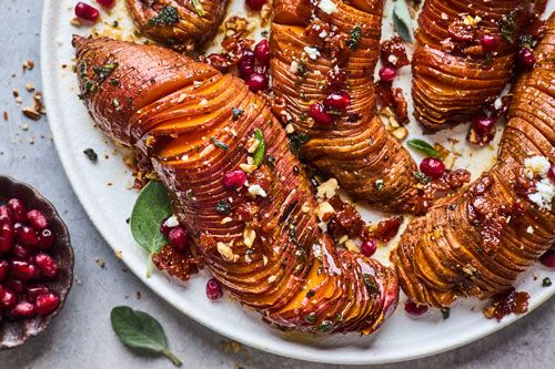 baked sweet potatoes with pomegranates and herbs on a white platter