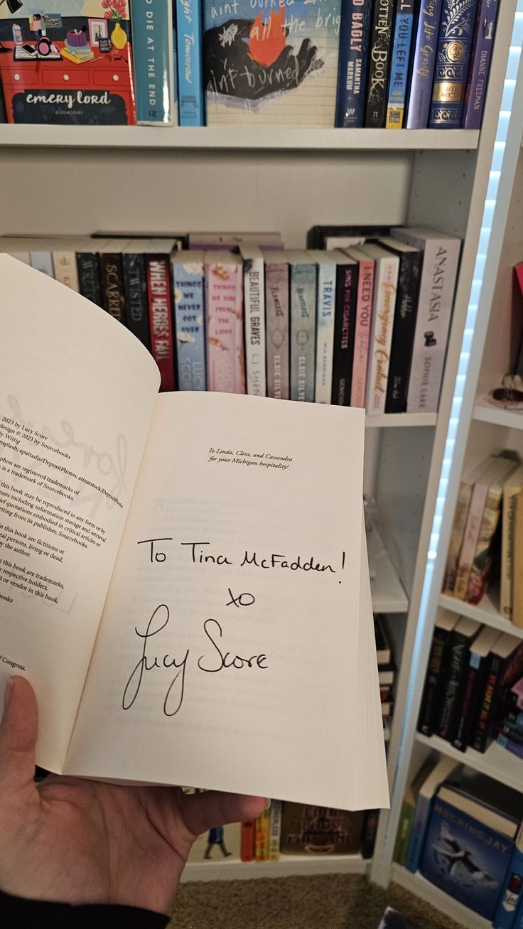 someone is holding an open book in front of a bookshelf full of books