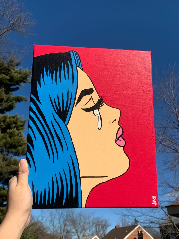 a person holding up a painting of a woman's face in front of some houses