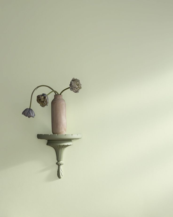 a pink vase sitting on top of a wooden shelf next to a wall mounted candle holder