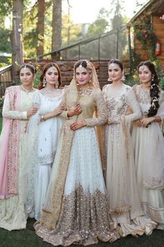 a group of women standing next to each other in wedding dresses and veils on the grass