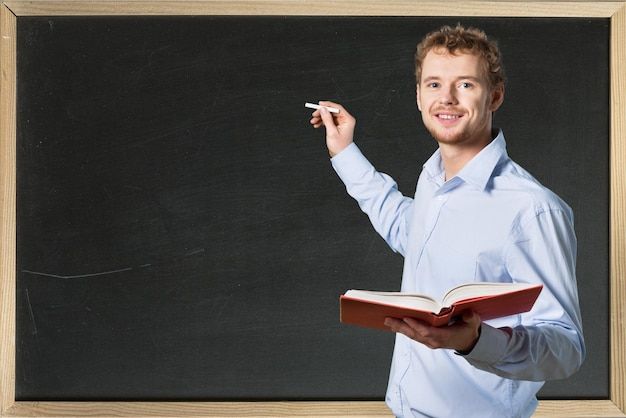 a man holding a book and writing on a chalkboard