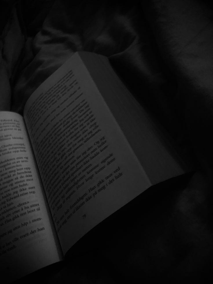 an open book sitting on top of a bed next to a black comforter and pillows