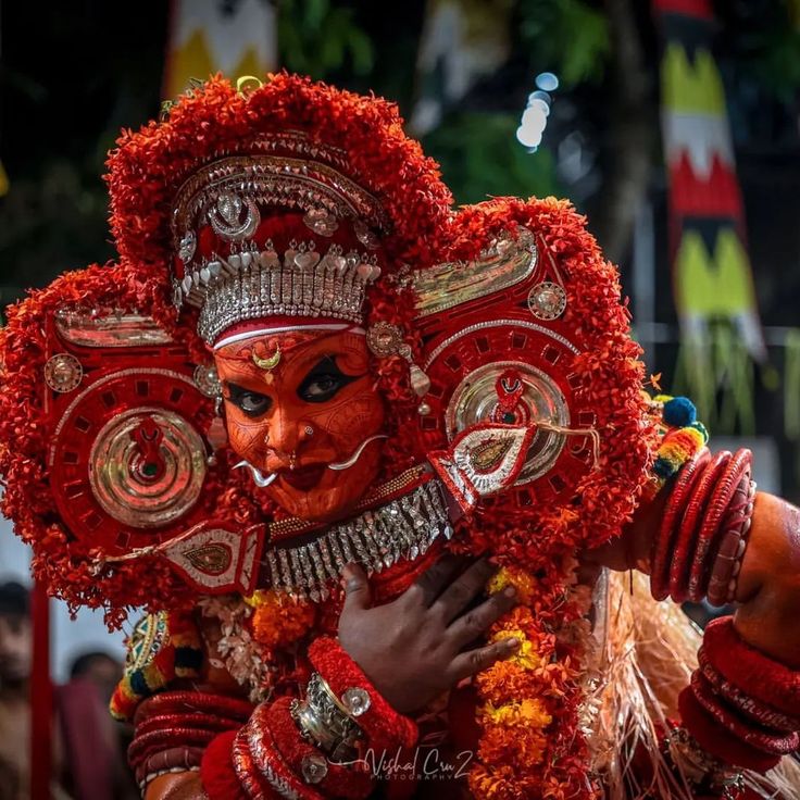 a man dressed in red and gold with his face painted like a mask, standing next to other people