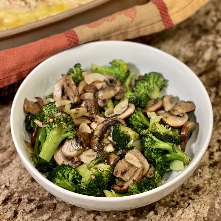 a white bowl filled with broccoli and mushrooms on top of a granite counter