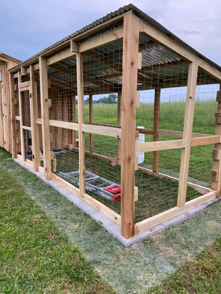 an outdoor chicken coop made out of wood and wire with grass in the back ground