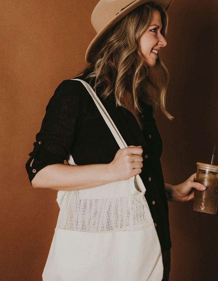 a woman wearing a hat and carrying a white bag with a straw in her hand