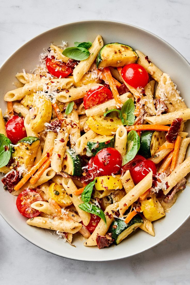 a white bowl filled with pasta, tomatoes and spinach on top of a marble table