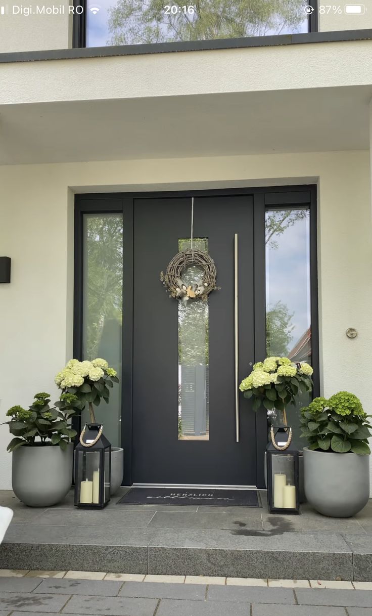 a black front door with two planters and a clock