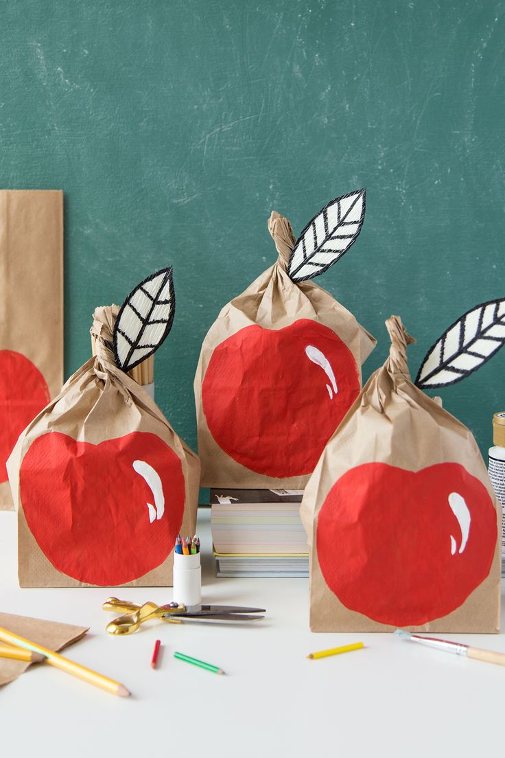 three bags with apples painted on them sitting on a table next to pencils and markers