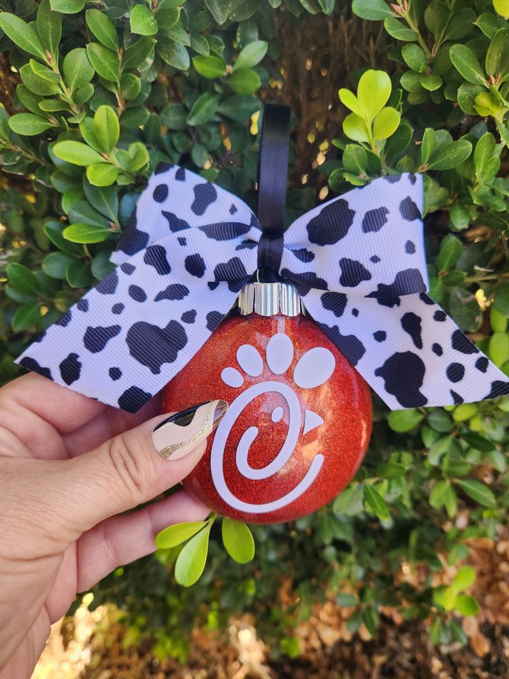 a hand holding an ornament with a dog's paw on it and a polka dot bow