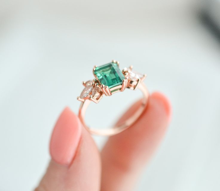 Few color schemes have a more sophisticated and luxurious feel than the iconic pairing between silver and emerald green – and this is a style we’ve captured in our stunning Ivy ring design. Simplistic yet beautiful, our Emerald ivy ring features a massive, 2.0-carat emerald as the main center, while six striking CZ crystals transform the look and create an unrivaled level of sophistication overall. ✦ DETAILS ✦✧ Handcrafted ✧ 2.0 Carat center stone✧ Emerald and cz crystals ✧ Sizes 3.75-11.25✧ Thi Elegant Emerald Princess Cut Ring For Proposal, Elegant Emerald Jewelry For Wedding Proposal, Elegant Three-stone Emerald Rings, Elegant Three Stone Emerald Rings, Elegant Emerald Three-stone Birthstone Ring, Emerald Jewelry With Princess Cut For Proposal, Rose Gold Solitaire Emerald Ring, Emerald Cut Rose Gold Birthstone Rings, Rose Gold Emerald Ring For Promise