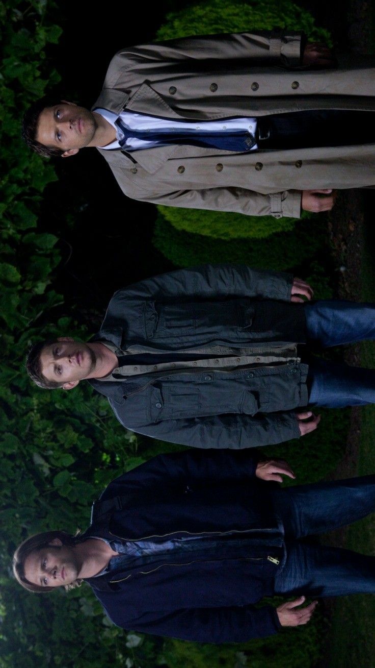 two young men standing next to each other in front of trees and bushes at night