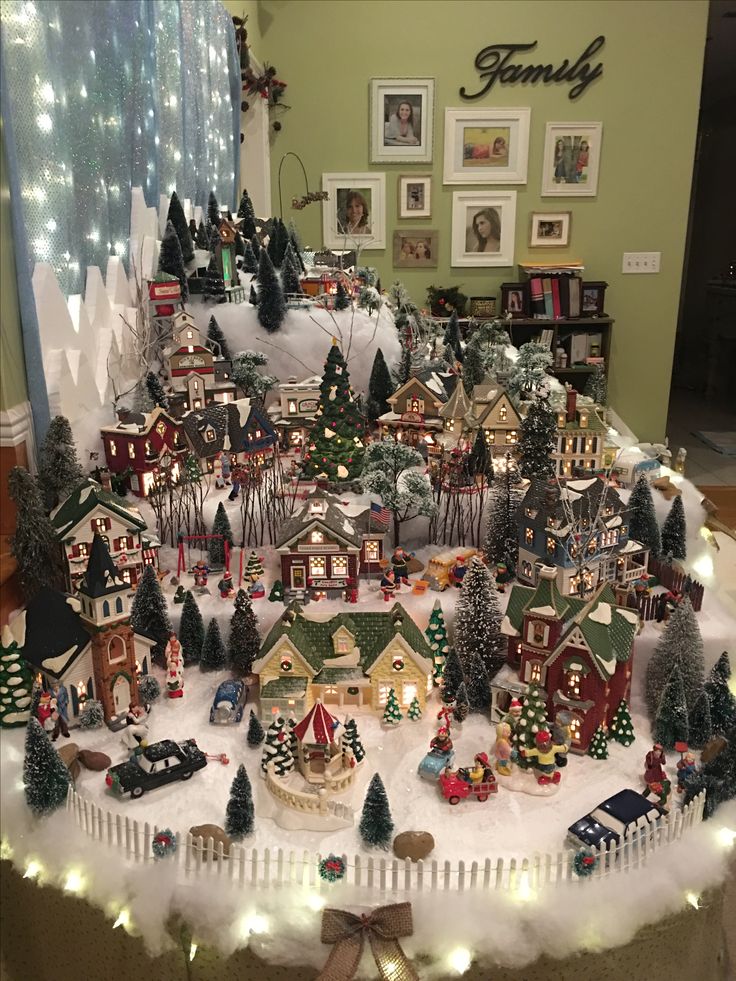 a christmas village is displayed on a table in front of a window with holiday lights