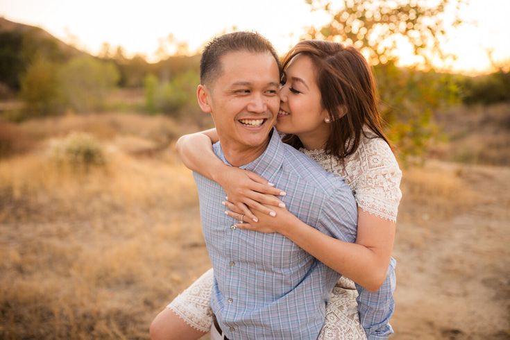 a man and woman hugging each other in the middle of an open field at sunset