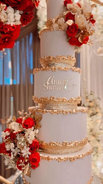 a three tiered wedding cake with red and white flowers on the top, surrounded by gold trimmings