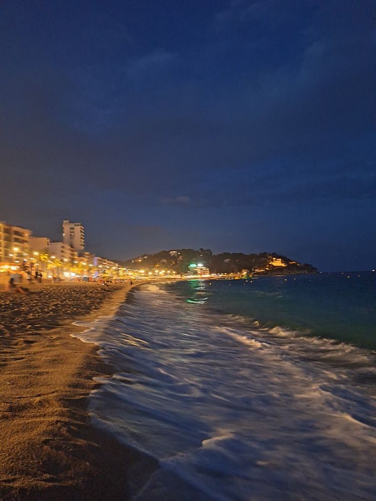 the beach is lit up at night with buildings in the background