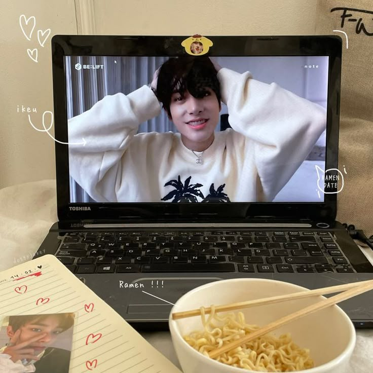 an open laptop computer sitting on top of a table next to a bowl of noodles