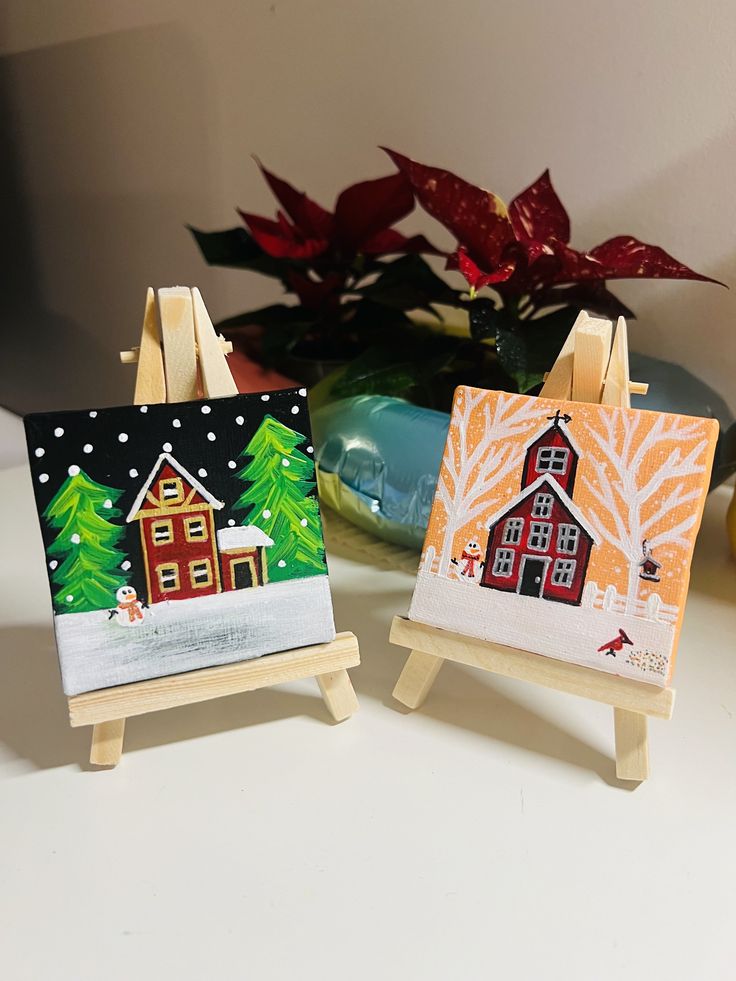 two easels with paintings on them sitting next to a potted plant