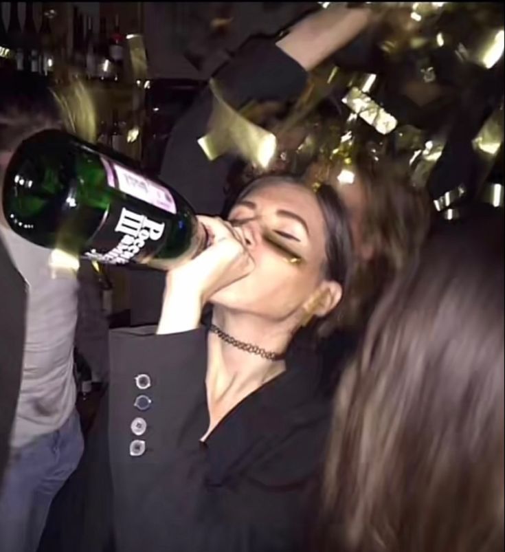 a woman drinking from a bottle while standing next to other people at a party with confetti in the air