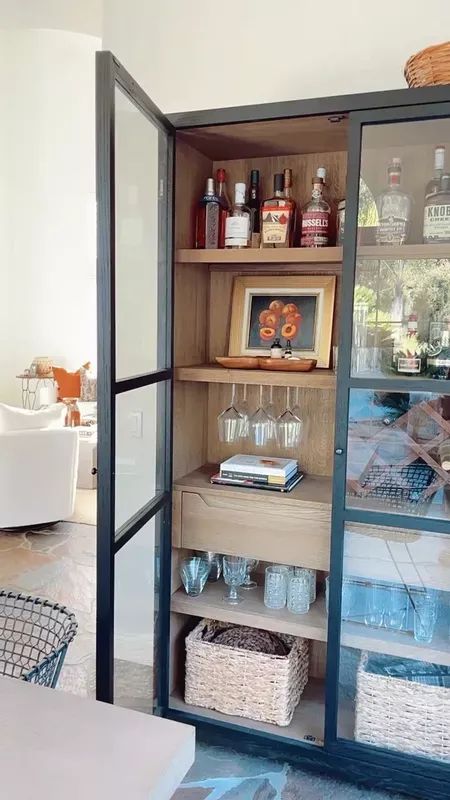 an open cabinet with wine glasses and bottles on it's shelves in a living room