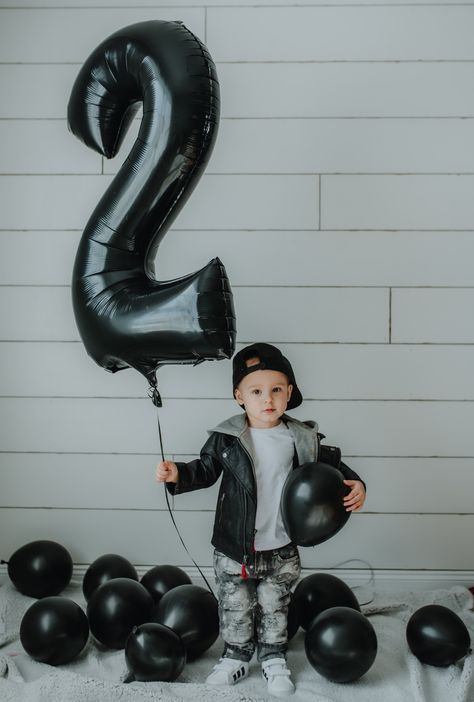 a young boy holding balloons in front of a number 2 sign and black balloons on the floor