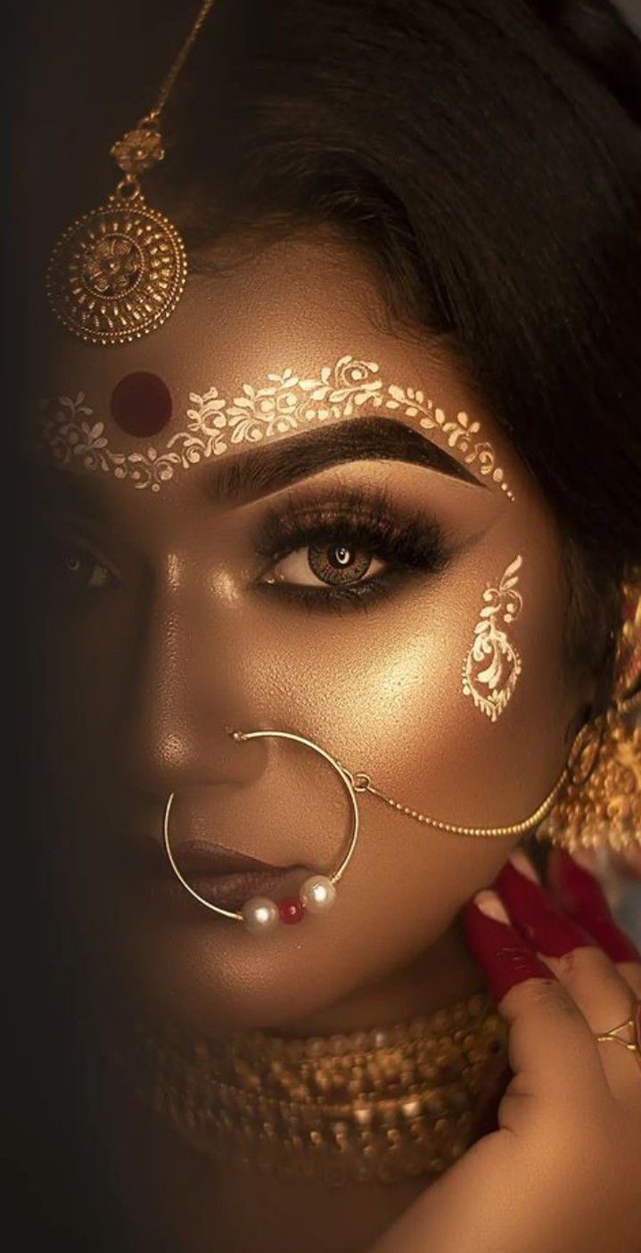 a woman wearing gold and red makeup with an elaborate nose ring on her head,