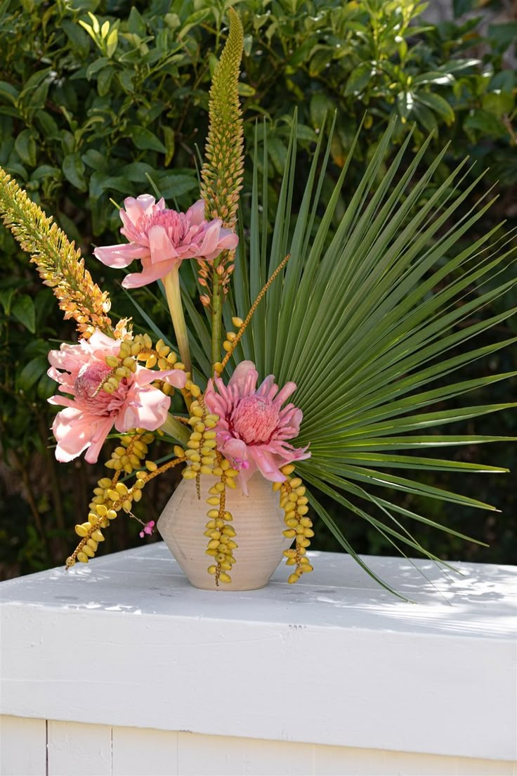 a vase filled with pink flowers sitting on top of a white table next to trees