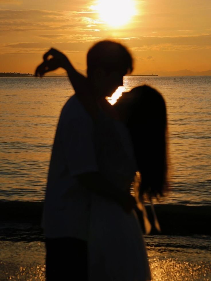 a man and woman standing next to each other near the ocean at sunset or sunrise