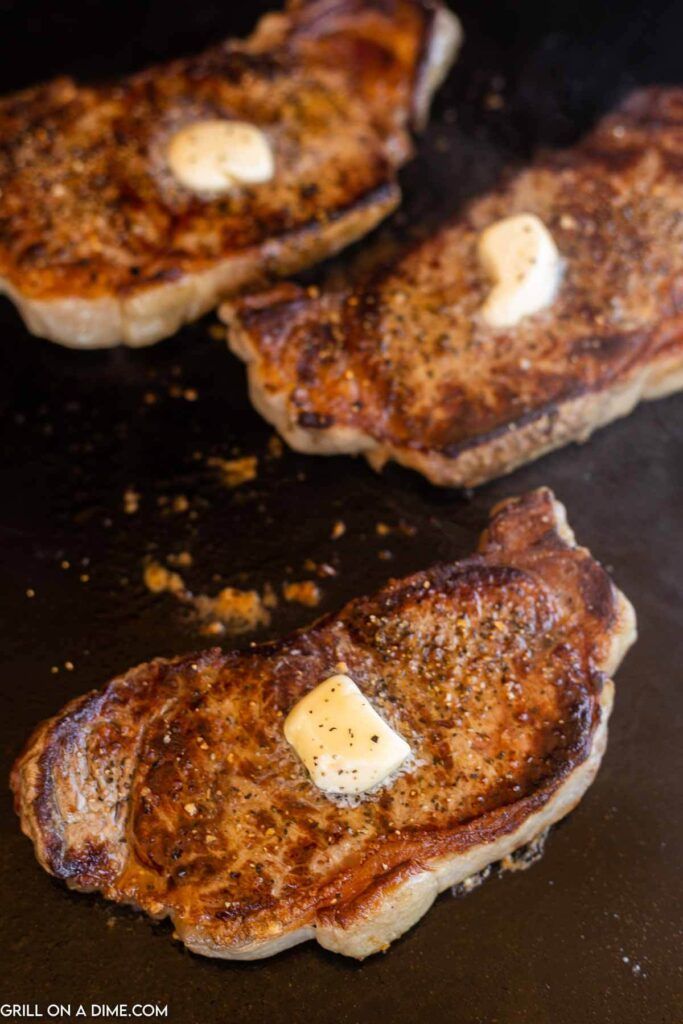 three steaks with butter on them cooking in a skillet