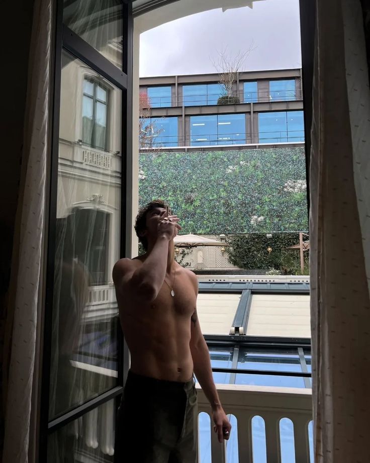 a shirtless man standing in front of an open window