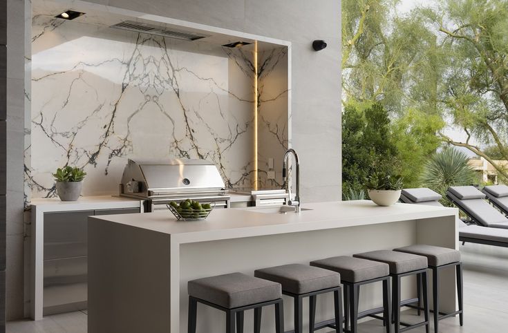 a modern kitchen with marble counter tops and stools next to an outdoor grill area