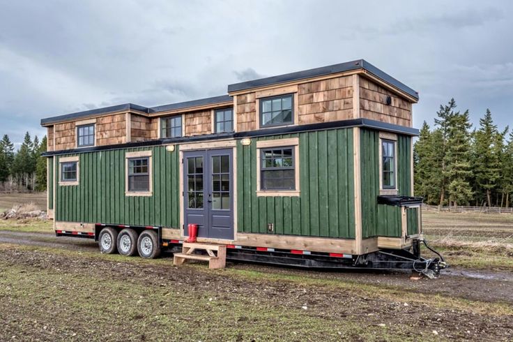 a green tiny house sitting on top of a trailer in the middle of a field