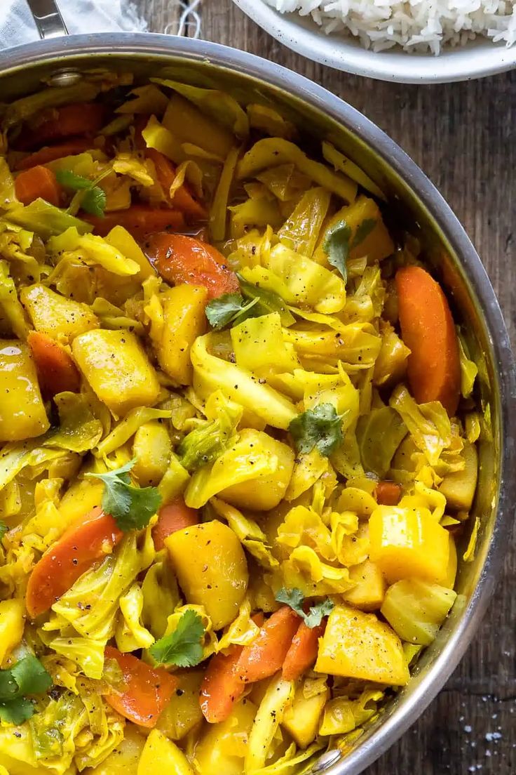 a pan filled with pasta and vegetables on top of a wooden table next to rice