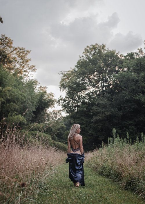 a woman walking down a path in the middle of a field with trees behind her