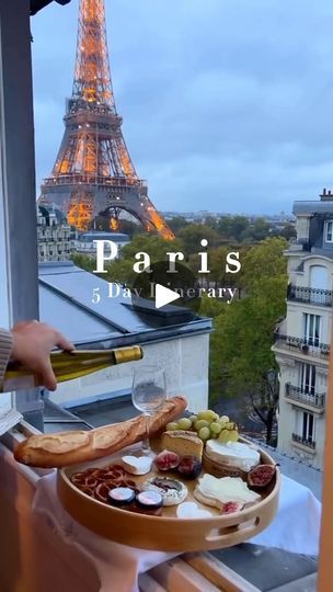 a person holding a bottle of wine near a tray with food on it and the eiffel tower in the background