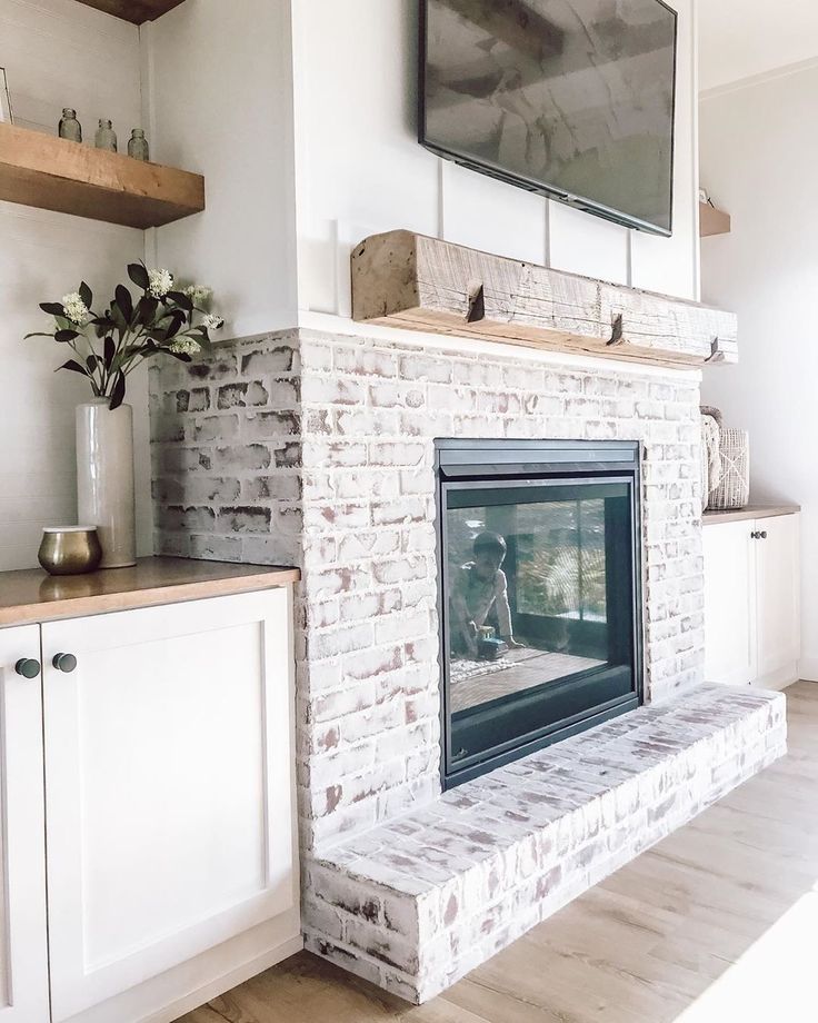 a white brick fireplace with a flat screen tv mounted above it's mantle and shelves