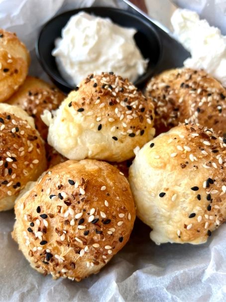 several rolls with sesame seeds on them and some cream cheese in the middle, sitting on wax paper