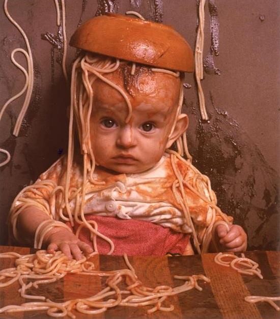 an old black and white photo of a baby with spaghetti on it's head