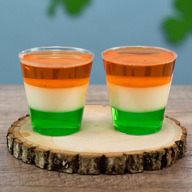 two glasses filled with colored liquid sitting on top of a wooden table next to each other