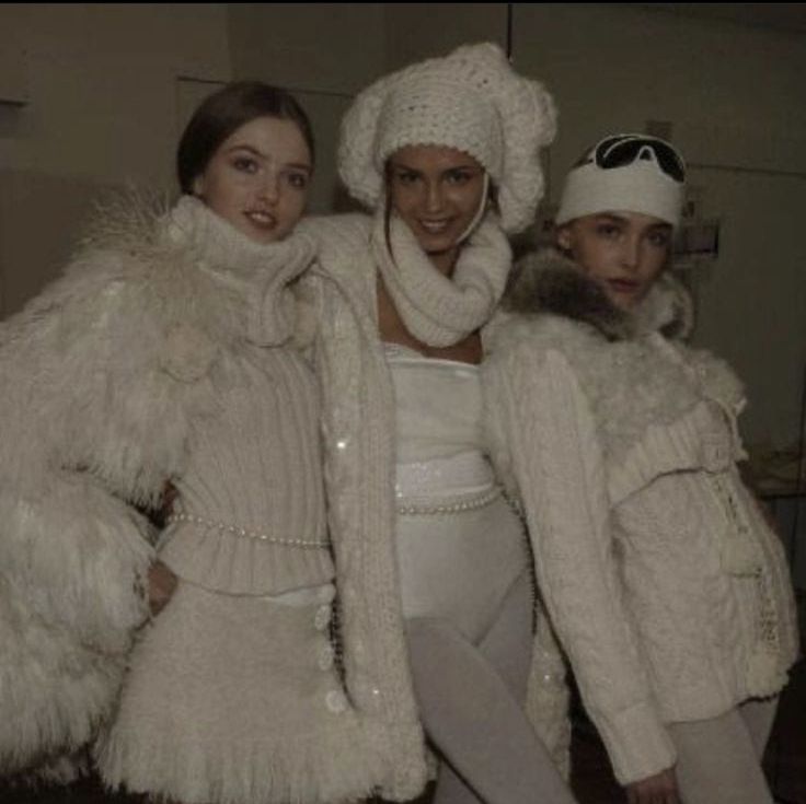 three women in winter clothes posing for the camera with one woman wearing a white hat and coat