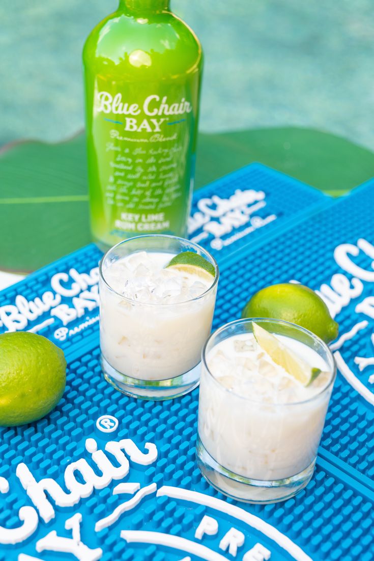 two shot glasses filled with ice and limes next to a bottle of booze