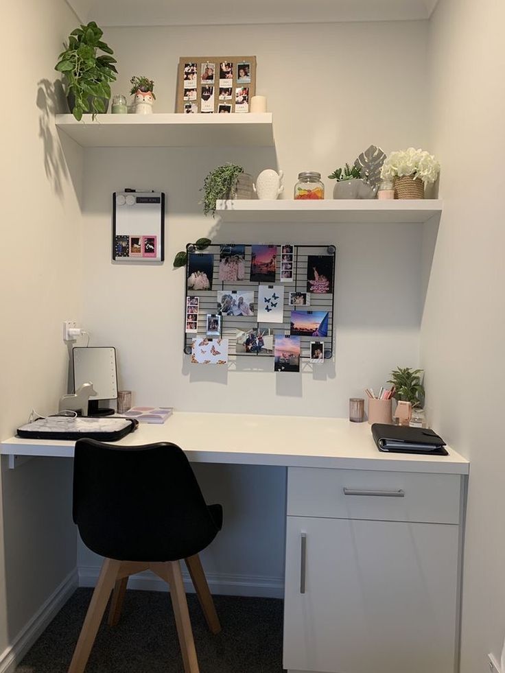 a white desk topped with a black chair next to a shelf filled with potted plants