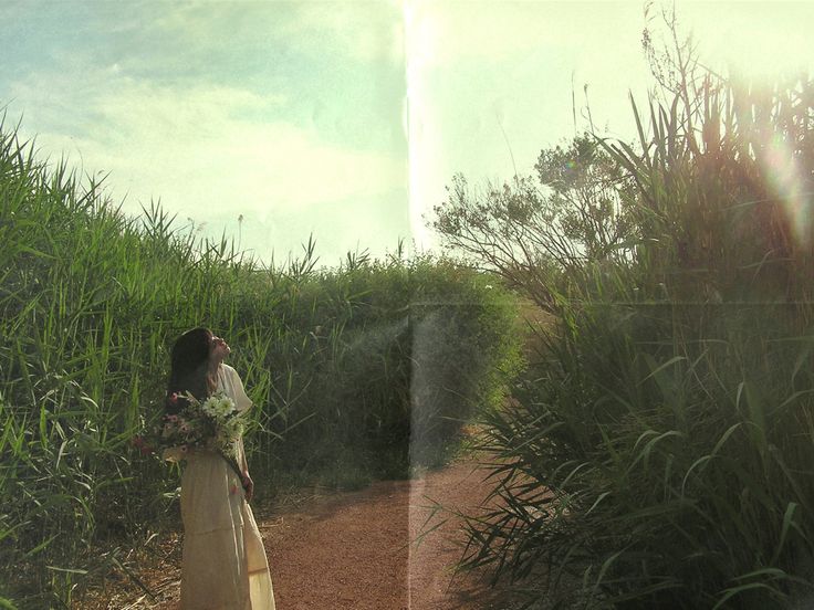 a woman standing on a dirt road next to tall grass