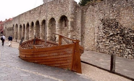 an old wooden boat sitting on the side of a brick road next to a stone wall